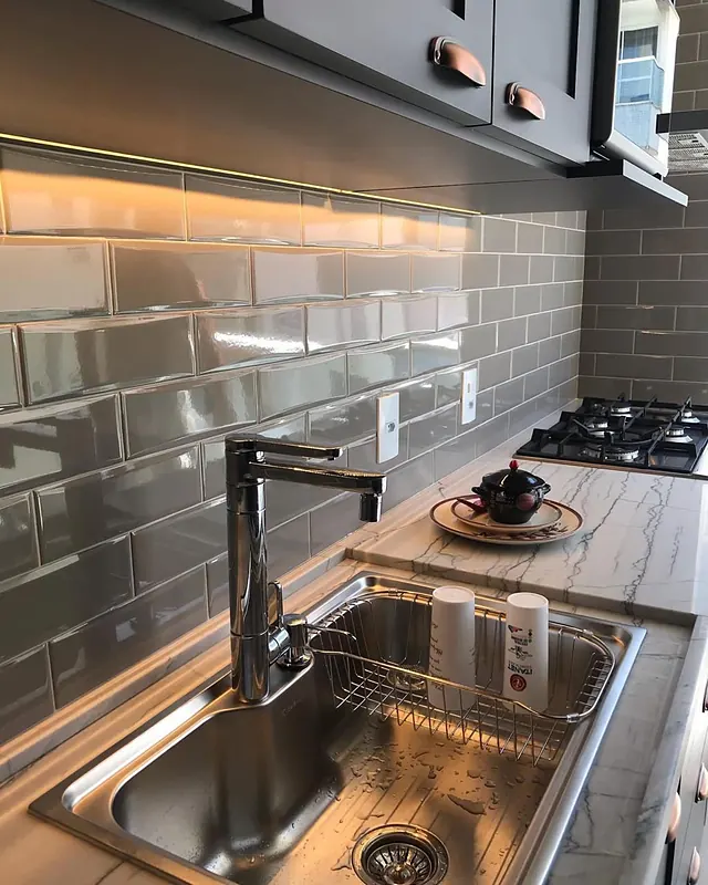 Bancada com cuba inox, revestimento metrô e iluminação sob os armários