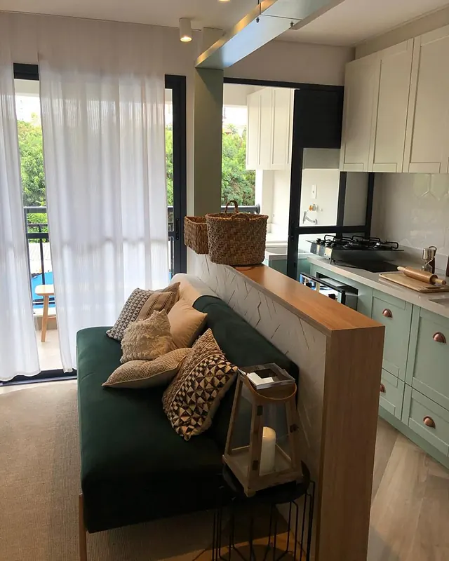 Sala de estar com sofá e almofadas, integrada à cozinha com armários verdes