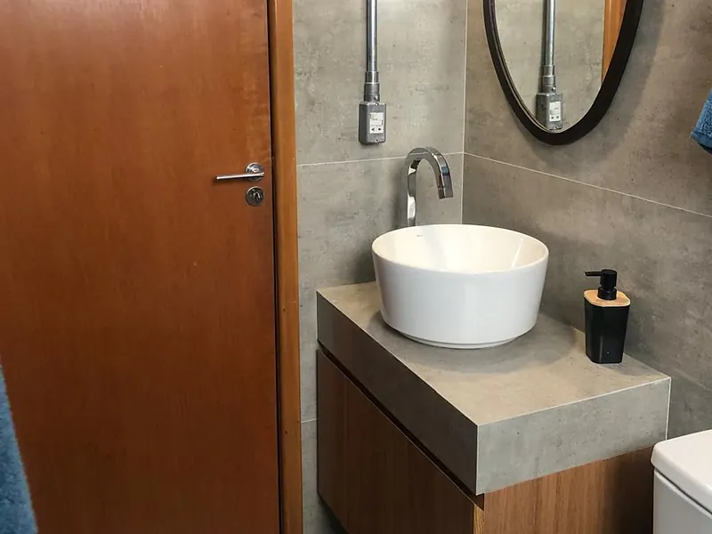 Lavabo com cuba redonda sobre bancada de pedra, gabinete de madeira e espelho redondo