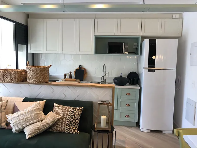 Sala ampla com sofá integrada à cozinha planejada com armários claros e geladeira