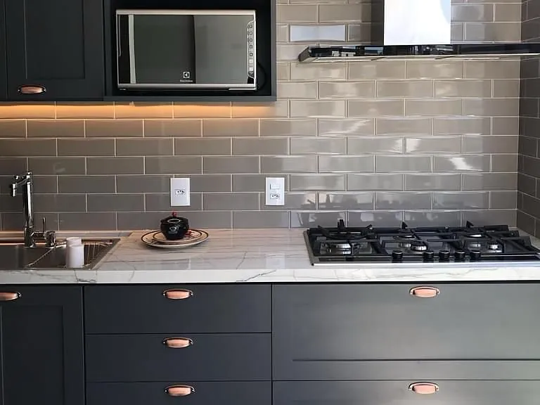 Cozinha com armários grafite, bancada em pedra, cuba, cooktop e revestimento metrô